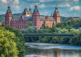 Im Hintergrund das Schloss Johannisburg in Aschaffenburg. In Bildmitte der Main mit der Willigesbrücke. Im weiteren Verlauf der Main mit einem Baum links am Bildrand