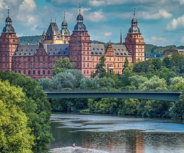 Im Hintergrund das Schloss Johannisburg in Aschaffenburg. In Bildmitte der Main mit der Willigesbrücke. Im weiteren Verlauf der Main mit einem Baum links am Bildrand