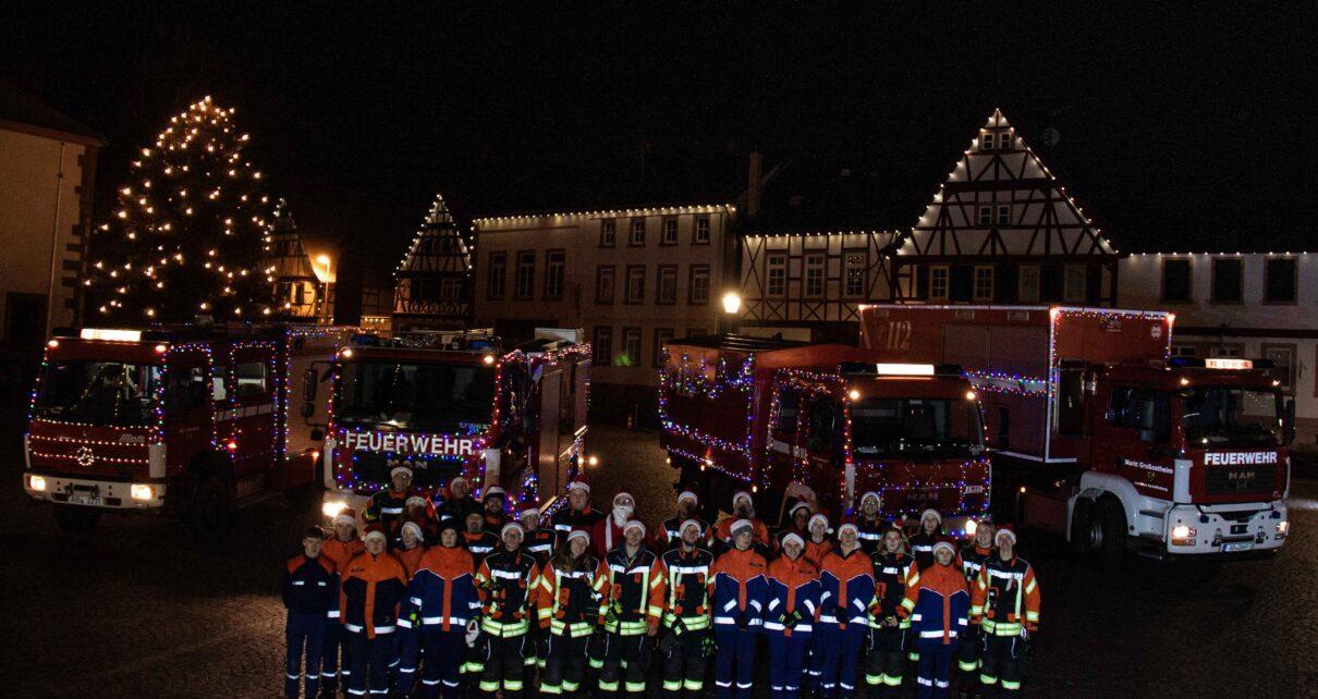 Festlich geschmückte Fahrzeuge der Feuerwehr Großostheim. Im Hintergrund das Nöthigsgut am Großostheimer Marktplatz. Davor stehen die Mitwirkenden der Feuerwehr Großostheim