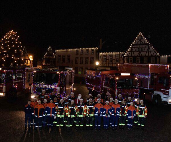 Festlich geschmückte Fahrzeuge der Feuerwehr Großostheim. Im Hintergrund das Nöthigsgut am Großostheimer Marktplatz. Davor stehen die Mitwirkenden der Feuerwehr Großostheim