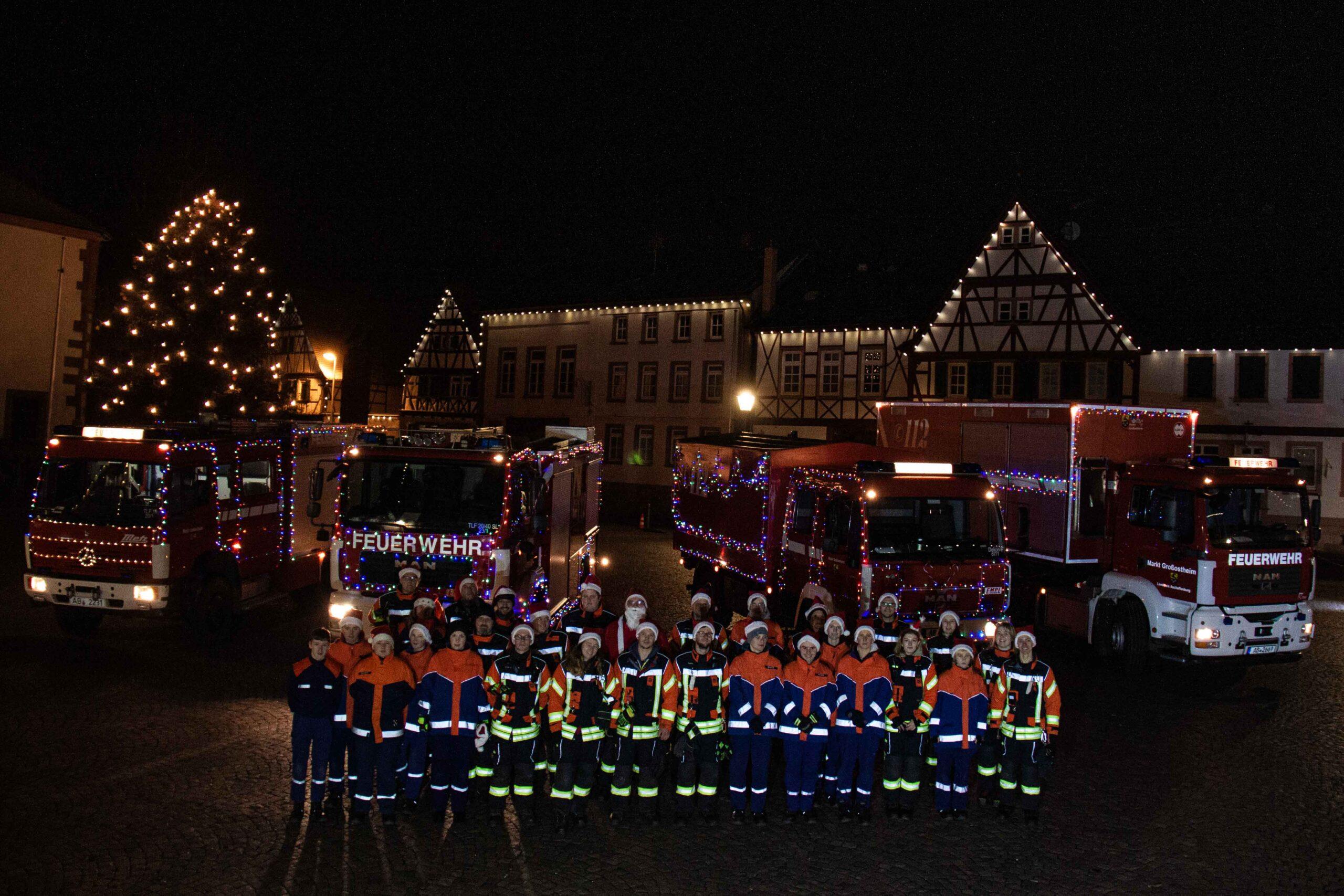 Festlich geschmückte Fahrzeuge der Feuerwehr Großostheim. Im Hintergrund das Nöthigsgut am Großostheimer Marktplatz. Davor stehen die Mitwirkenden der Feuerwehr Großostheim