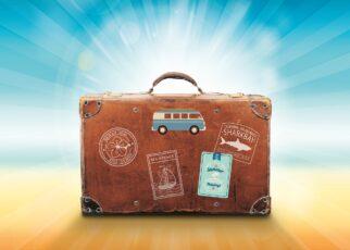 Alter Koffer mit Aufklebern auf einem Sandstrand und blauem Himmel