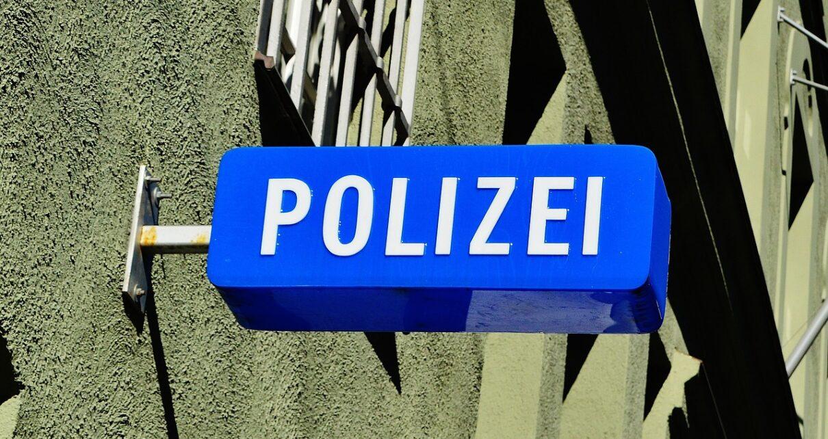 Blaues Schild an eine Hauswand mit vergitterten Fenster geschraubt, mit der Aufschrift Polizei