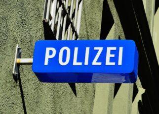 Blaues Schild an eine Hauswand mit vergitterten Fenster geschraubt, mit der Aufschrift Polizei