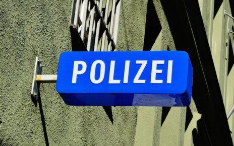 Blaues Schild an eine Hauswand mit vergitterten Fenster geschraubt, mit der Aufschrift Polizei