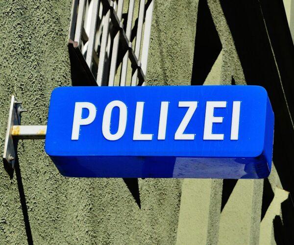 Blaues Schild an eine Hauswand mit vergitterten Fenster geschraubt, mit der Aufschrift Polizei