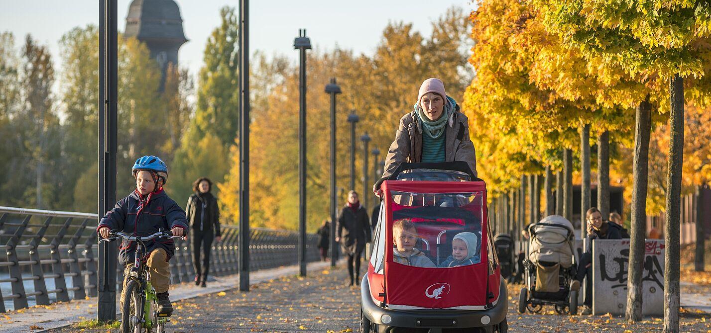 Kind auf dem Fahrrad und Lastenrad mit Kindern auf einem herbstlichen Radweg